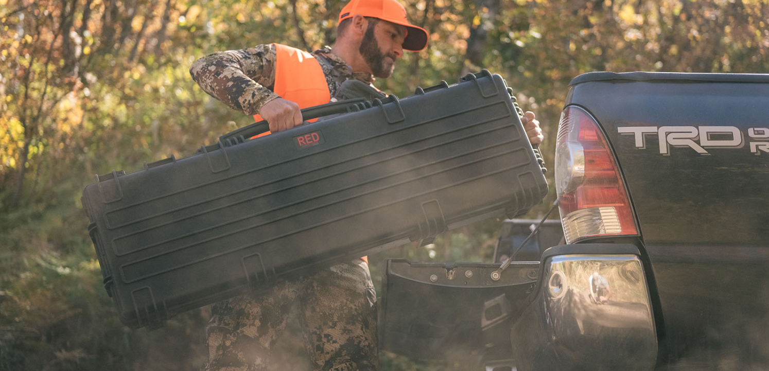 A man carrying a large explorer long gun case on his back while going inside a car.