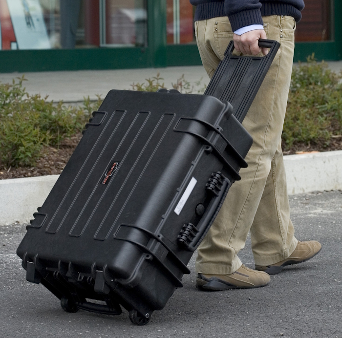 5823.B TROLLEY A man drags a large black suitcase on wheels, identified as "Explorer gun case 5823," while walking in an urban setting.