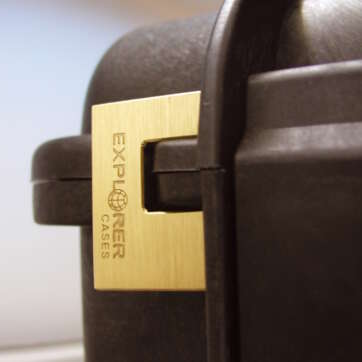 Detailed view of a black suitcase adorned with a gold explorer padlock, emphasizing its stylish and secure appearance.