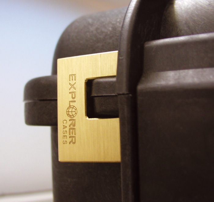 EXPL PADLOCK Detailed view of a black suitcase adorned with a gold explorer padlock, emphasizing its stylish and secure appearance.